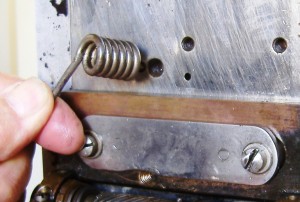 Locate the short end of the spring and guide it into the end holding hole which is left of the centre fixing screw hole